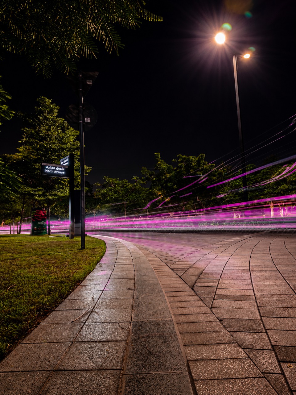 Pink light trails along a wet city path at night